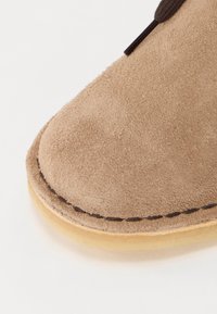 Beige mokkasinsko nærbilde, rund tupp, sydd mørkebrune detaljer og en lys tan gummisåle med en glatt finish.
