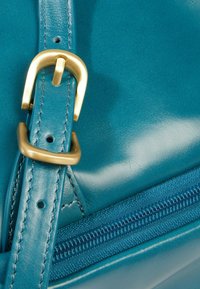 Groene leren handtas met een gladde textuur, voorzien van een gouden metalen gesp en een zichtbare ritssluiting langs de rand.