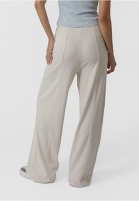 Pantalons larges en tissu beige clair, avec une texture lisse et des coutures verticales, associés à des chaussures à motifs.