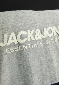 Siva majica s natpisom "JACK & JONES ESSENTIALS" u bijelim, teksturiranim slovima, s ležernim krojem i mekanom tkaninom.