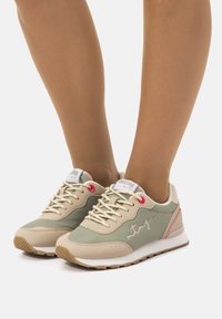 Sneaker im hellbeigen und grünen Farbschema. Glattes Leder und textile Materialien, akzentuiert mit pinken Details und gesticktem Logo.