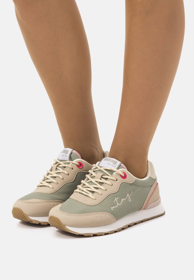 Sneaker im hellbeigen und grünen Farbschema. Glattes Leder und textile Materialien, akzentuiert mit pinken Details und gesticktem Logo.
