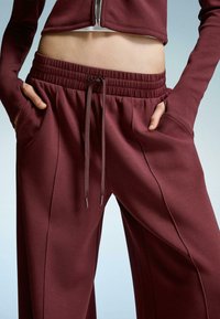 Bordeauxkleurige sweatpants met een elastische tailleband, aantrekkoord en zijzakken. Soepele textuur met verticale naaddetails.