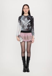 Long-sleeve top with black and blue graphic patterns, pink shorts with frayed edges, and knee-high black boots, holding a silver handbag.