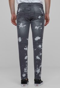 Jeans ajustados en denim gris oscuro con patrones de salpicaduras blancas. Cuenta con cinco bolsillos y una cintura estándar. Textura suave.