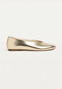 Chaussure plate dorée métallique avec bout pointu et petit talon, dessus en cuir lisse et brillant, vue de côté sur fond uni.