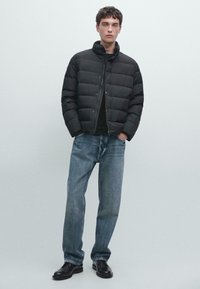 Black puffer jacket with a high collar, snap fastening, and quilted design, paired with blue straight-leg jeans and black shoes.
