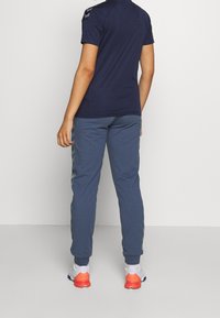 Marinblus med kort ärm i kombination med ljusblå träningsbyxor med sidosträck och vita skor med orange detaljer. Enkel atletisk design.