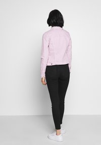 Chaqueta de mezclilla rosa claro con un diseño ajustado, cierre de botones y mangas largas, combinada con jeans skinny negros y zapatillas blancas.