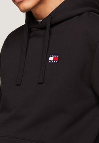 Felpa nera con cappuccio in cotone, con un piccolo logo ricamato "TOMMY JEANS" in rosso e bianco sul petto, e lacci piatti.