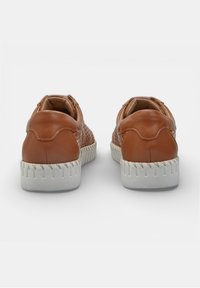 Zapatos marrones de cuero tipo slip-on con suelas de goma blanca, costuras visibles y laterales perforados, mostrados desde atrás sobre un fondo blanco.