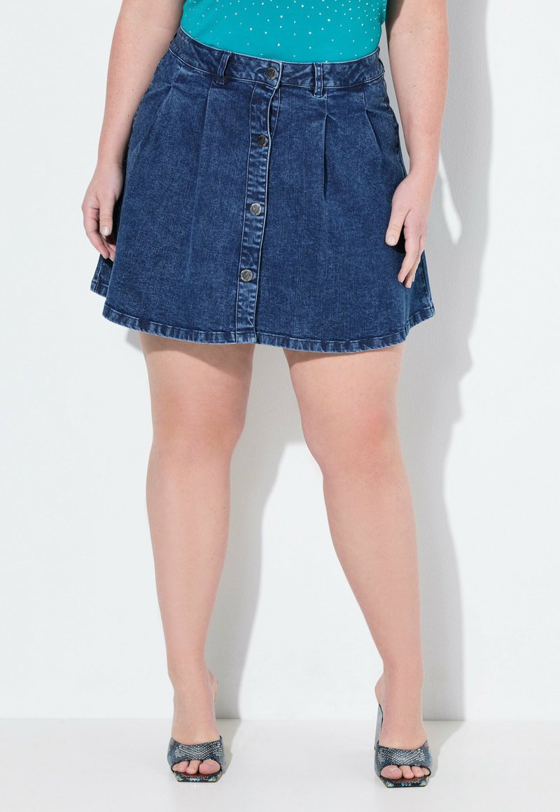 Jupe en denim bleu foncé, dotée d'une fermeture à boutons à l'avant, de plis et d'un ourlet évasé. Texture lisse avec des coutures visibles le long des bords.