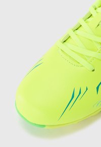 Neon žlté futbalové topánky s modrými akcentovými pruhmi, hladkým syntetickým zvrškom a plochými šnúrkami. Zaoblená špička a textúrovaná podrážka pre trakciu.
