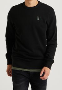 Felpa nera con colletto e polsini a costine. Presenta una scritta verde sul petto. Tessuto morbido, vestibilità rilassata, adatta per un look casual.
