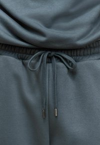 Pantalones jogger de color gris oscuro, confeccionados en un tejido suave, con cintura elástica, cierre con cordón y puntas metálicas en el cordón.