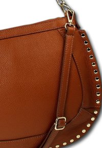 Braune Leder-Schultertasche mit glatter Textur, geschwungener Form und goldenen Nieten an der Seite, mit abnehmbarem Tragegurt.