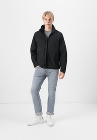 Black zip-up jacket with hood, featuring a smooth texture and lightweight fabric. Paired with light blue jeans and white sneakers.
