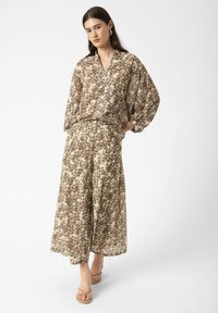 Completo marrone e crema con motivo, composto da una blusa ampia e pantaloni a gamba larga, realizzati in tessuto leggero, con scollatura a V e maniche a palloncino.