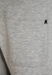 Szary materiał o teksturowanym wykończeniu. Posiada kieszeń z starannie obszytym brzegiem oraz małym czarnym akcentem w postaci logotypu "R".