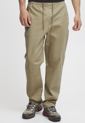 Beige drawstring pants with a relaxed fit, crafted from a smooth, lightweight fabric; paired with grey and black hiking shoes.