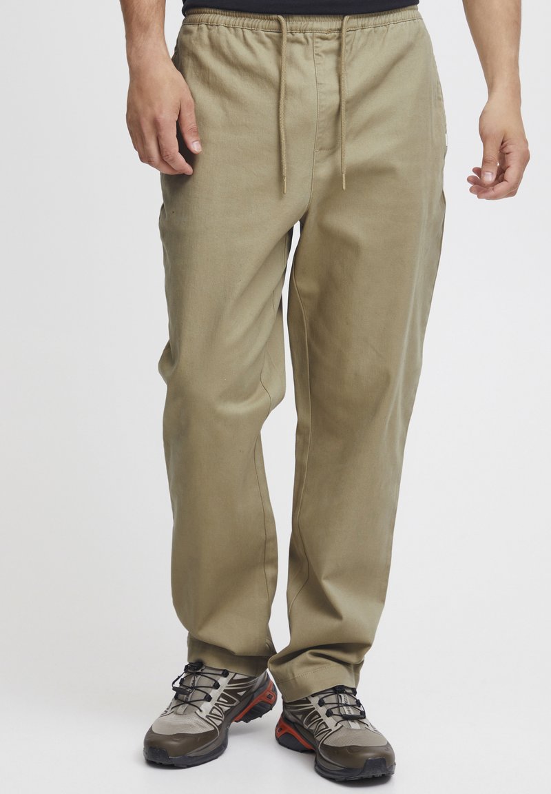 Beige drawstring pants with a relaxed fit, crafted from a smooth, lightweight fabric; paired with grey and black hiking shoes.