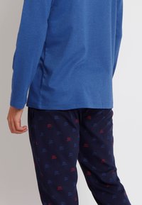 Camisa de manga larga azul combinada con pantalones marinos que presentan un patrón de texto repetido en rojo y azul, fabricada en suave material de algodón.