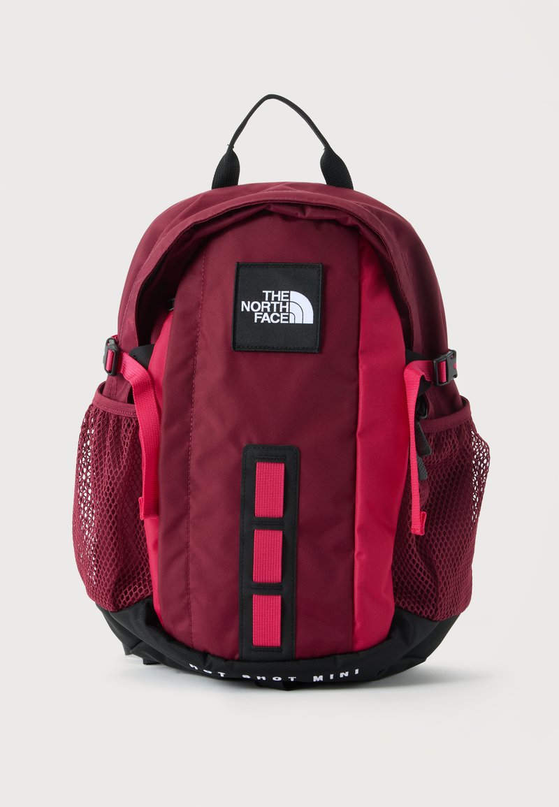 Κόκκινο και βουργουνδί σακίδιο πλάτης North Face με μαύρο λογότυπο, πλαϊνές τσέπες από δίχτυ και μαύρη χειρολαβή σε λευκό φόντο.