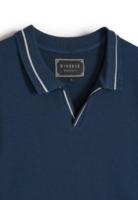 Granatowa koszulka polo o teksturowanym splocie. Posiada klasyczny kołnierzyk z szarymi paskami oraz metkę z napisem "Diverse", rozmiar L.