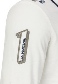 Bílé dlouhé rukávy s ozdobnou vyšívanou číslicí "1" v šedé a modré barvě na horní paži, s texturovanou tkaninou.