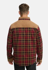 Rood en zwart geruite blouse met een beige corduroy schouderstuk en manchet. Beschikt over lange mouwen en knoopsluitingen op de manchet. Achteraanzicht.