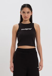 Svart kort tanktopp laget av ribbestrikket stoff, med hvit "lowlights" logo foran, kombinert med svarte joggebukser.