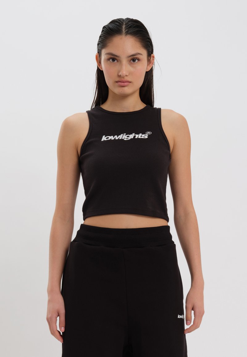 Svart kort tanktopp laget av ribbestrikket stoff, med hvit "lowlights" logo foran, kombinert med svarte joggebukser.