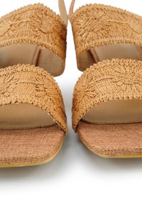 Vlechtst straw slipper in karamelkleur, met een platte geweven textuur en een brede voetbed. Versterkte randen en minimalistische ontwerpelementen.