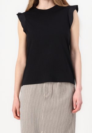 Woman wearing a black sleeveless top with ruffled shoulder details and a beige skirt with vertical black stripes.