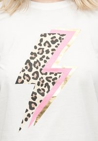 Λευκό μπλουζάκι με μεγάλο σχέδιο αστραπής, γεμάτο με τύπωμα λεοπάρ και περιγράμματα σε ροζ και μεταλλικό χρυσό.