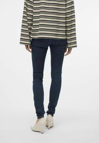 Raišotu garo piedurknu topiņš apvienots ar tumši ziliem skinny džinsiem un baltām platformām, parādot ikdienišķu stilu un pieguļošu siluetu.