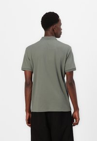 Mørkegrønn polo-skjorte med korte ermer og ribbestrikket krage. Glatt tekstur, rett snitt og subtil detaljering ved ermekanter.