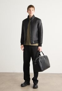 Melnā pūkains jaka ar augstu apkakli, zaļa krekla zemāk, brīvi pieguļoši melni bikses un melna ādas soma ar rokturiem. Gluda tekstūra.