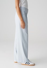 Pantalons larges bleu clair avec une taille haute et des plis à l'avant, associés à des baskets blanches avec des accents navy et une semelle en gomme.