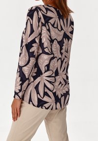 Pitkähihaisessa paidassa on tummansininen tausta ja suuria vaaleanbeigejä kukkakuoseja. Sujuva kangas, pyöristetty helma ja rento istuvuus.