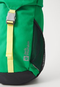 Roheline ja must seljakott kollase rihma ja halli klambriga, musta võrgust küljetasku ja halli "Jack Wolfskin" logoga.