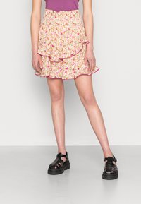 Saias mini florais com uma palete de cores rosa e amarelo, bainha com volutas e cintura elástica; combinadas com sapatos de plataforma pretos e com tiras.