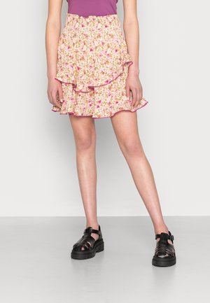 Saias mini florais com uma palete de cores rosa e amarelo, bainha com volutas e cintura elástica; combinadas com sapatos de plataforma pretos e com tiras.