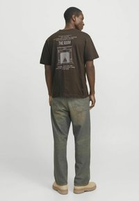 Brown cotton t-shirt featuring a graphic on the back, paired with light green denim pants and beige boots. Simple design, relaxed fit.