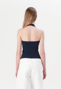 Marineblauwe haltertop gemaakt van rekbare stof, met een aansluitend ontwerp en een gladde textuur; model draagt een witte wijde broek.