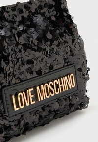 Primo piano di un tessuto in paillettes nere con lettere dorate "LOVE MOSCHINO" imprese su una toppa in pelle nera.