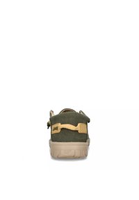 Scarpa canvas verde con suola in gomma beige, dotata di una cinghia posteriore, tessuto testurizzato e design minimalista. La vista posteriore mostra una costruzione robusta.