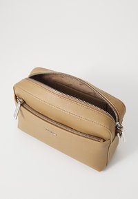 Sac en cuir beige à fermeture éclair avec une texture lisse, à double compartiments et avec des accents en métal argenté, comportant un logo sur le devant.