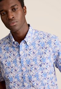 Kortebloesem overhemd met knopen in lichtblauw met witte en paarse bladenpatronen, voorzien van een standaard kraag en witte knopen.