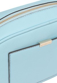 Lichtblauwe leren pouch met een gouden rits, plat ontwerp, rechthoekige vorm en een eenvoudig metalen label met de merknaam.